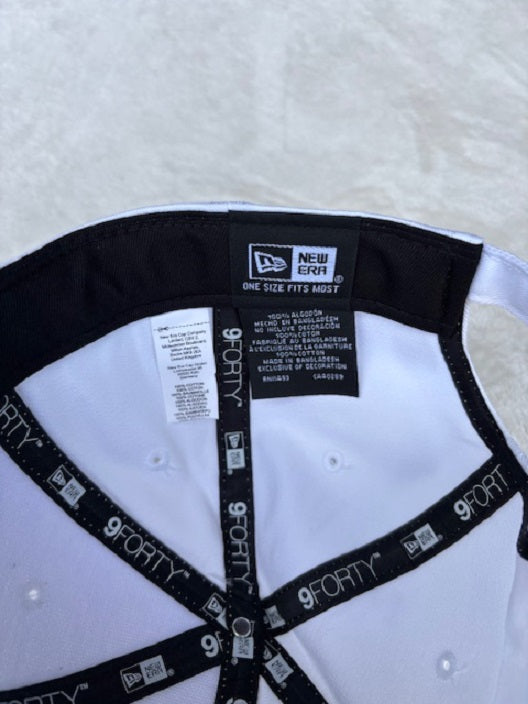 Close-up of the inside back of a white New Era cap, showing the black and white interior band, New Era brand label, size information tag, and black adjustable strap with white 9FORTY text.